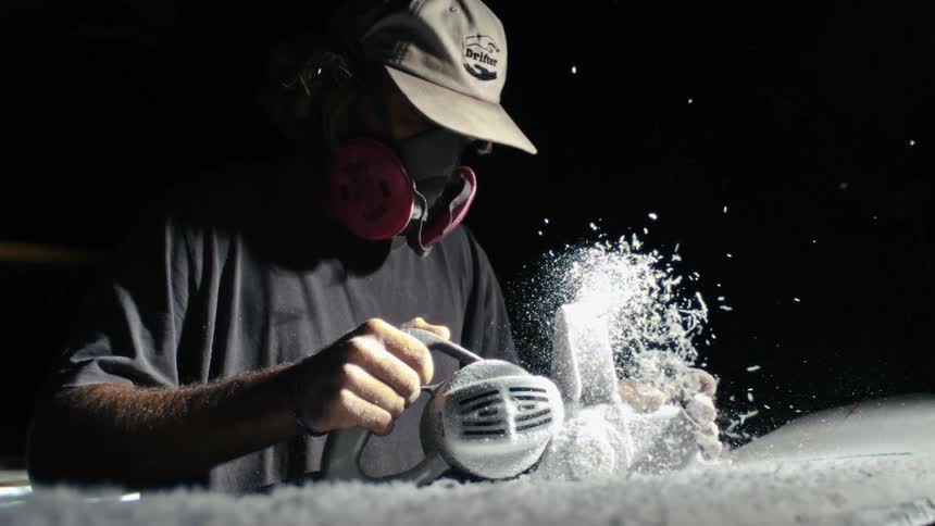 Man wearing a protective breathing mask fills the area with white particles while using a power tool on a surface