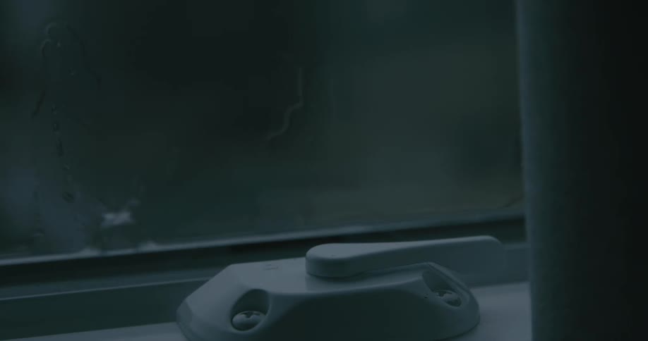 Rain splashes against fogged glass as a metal window latch rests in low light framed by streaks of condensation