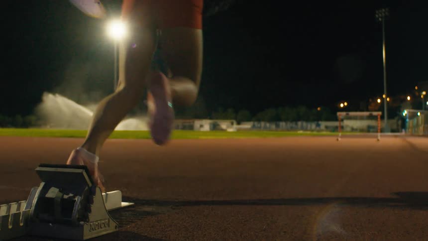 A young woman is practicing running on a track at night taking off on a solo run