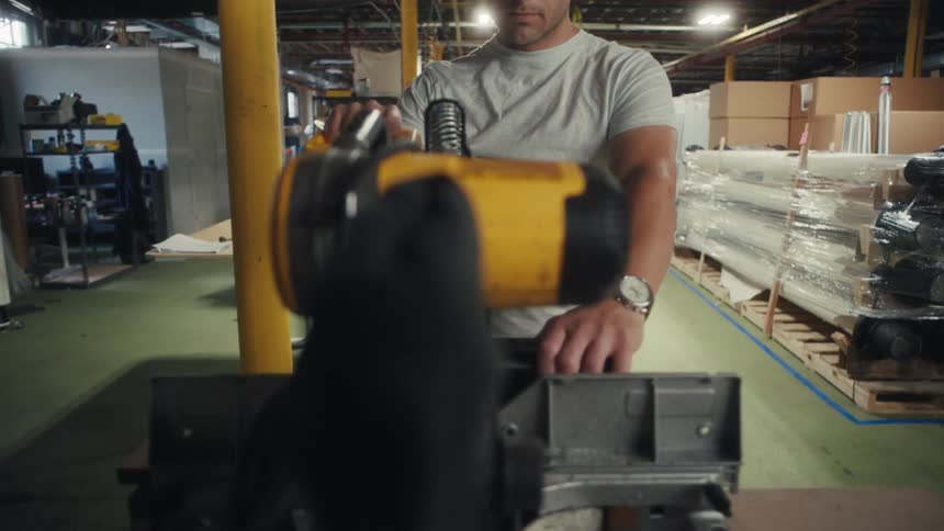 The worker is using a table saw in the factory