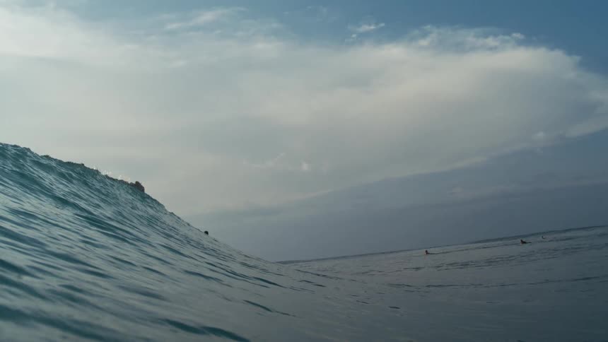 Surfers sit atop gentle ocean swells as they wait for the next wave under a cloudy sky