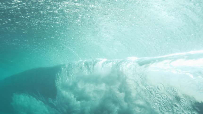A dramatic underwater wave curls illuminated by sunlight filtering from above