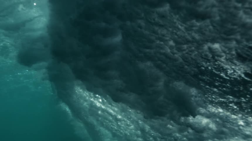A whale or boar gliding along the water near the surface creating waves and bubbles