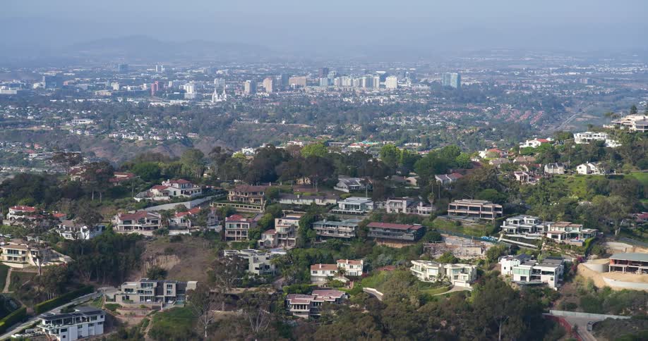 A panoramic view of luxury homes on a hillside with a sprawling cityscape in the background