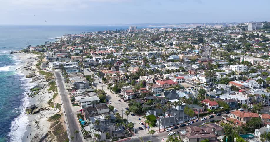 The video presents a scenic aerial view of a sprawling coastal city with numerous houses nestled on hillsides a long sandy beach and ocean are visible in the background under a sunny sky