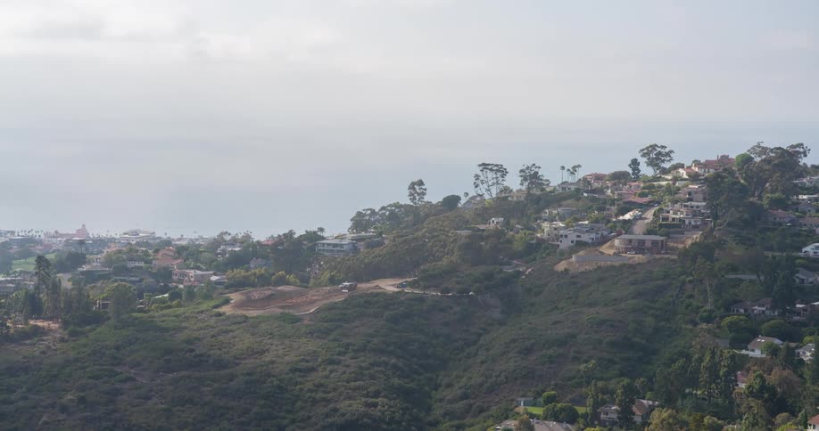Hillside homes nestled among lush greenery with a distant view of the ocean under a hazy sky