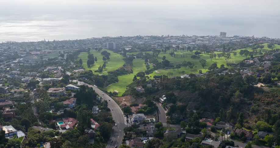 A large golf course stretches through a lush urban area near the coast surrounded by residential neighborhoods