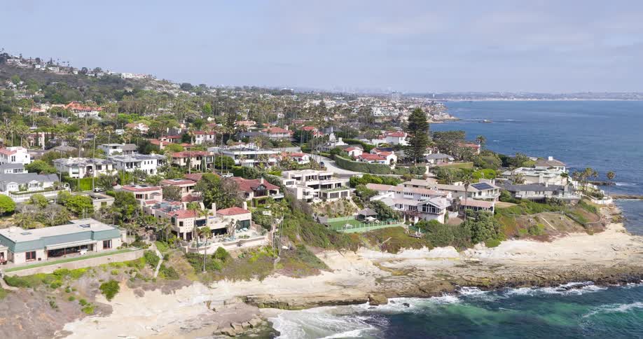 Urban waterfront with upscale homes on the waterfront and waves crashing against the rocks on a sunny beach