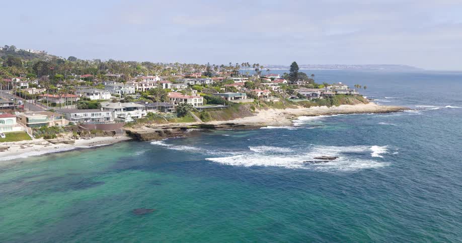 Coastal homes line a scenic rocky shoreline with turquoise waters and palm trees dotting the neighborhood