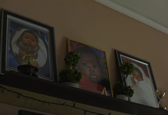The video displays a shelf adorned with framed pictures of babies interspersed with small green plants in pots and decorative hourglasses the setting appears to be indoors with a plain wall as the background