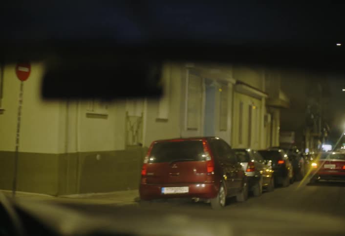 A view from inside a car looking out a blurred windshield at a dimly lit urban street scene