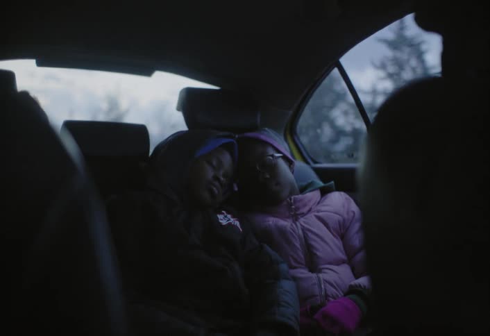 Two girls lying down hugging each other in a moving car