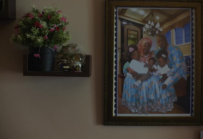 A picture frame of a family with three kids on their laps hangs on a wall with a flower vase positioned beside the frame