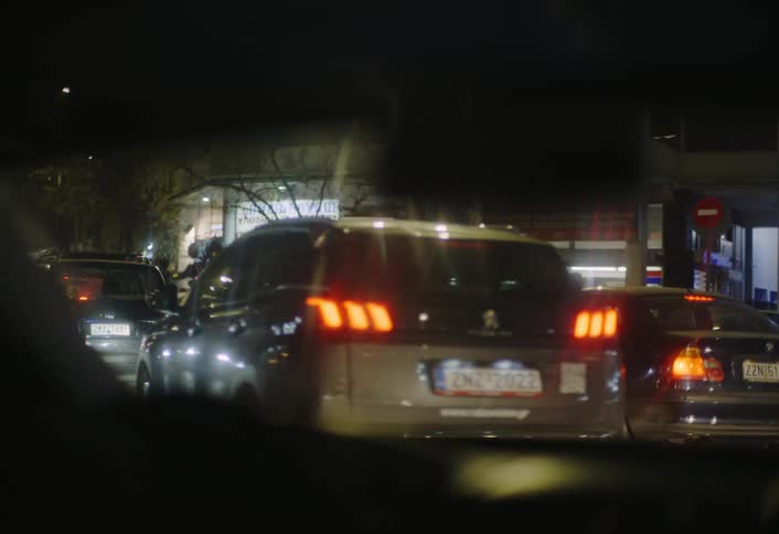The video shows a night scene from inside a car with the reflections of streetlights and car lights visible on the windshield several cars are seen ahead their taillights glowing red suggesting a city street or traffic at night