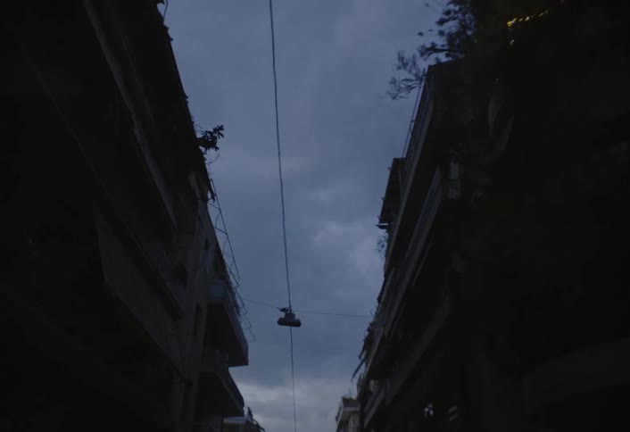 A city street is lined with buildings on each side with a power line running down the middle of the street on a cloudy evening
