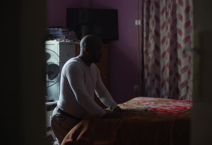 Man kneeling in a bedroom pressing his hands into a mattress on the bed