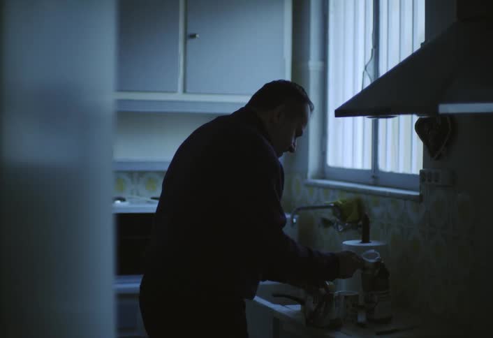 A man is in the kitchen by the sink preparing coffee