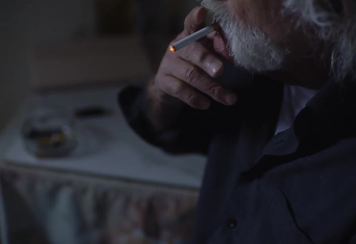 A person with a white beard lighting a cigarette and taking a puff