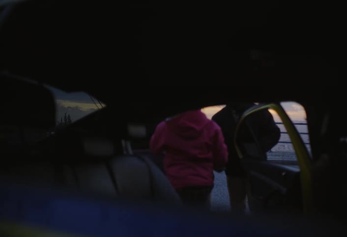 Parents silhouetted against a bright ocean sunset walk toward a dark car to take out their children so they can watch the view together