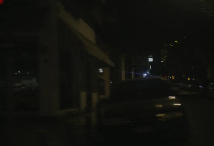 A blurry night time journey through a city street with various illuminated storefronts and passing vehicles visible