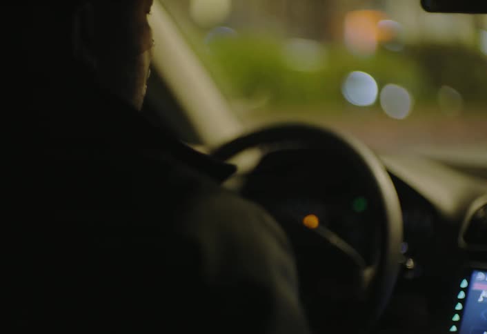 A driver is barely visible in low light with only the faint glow of outside streetlights illuminating the scene