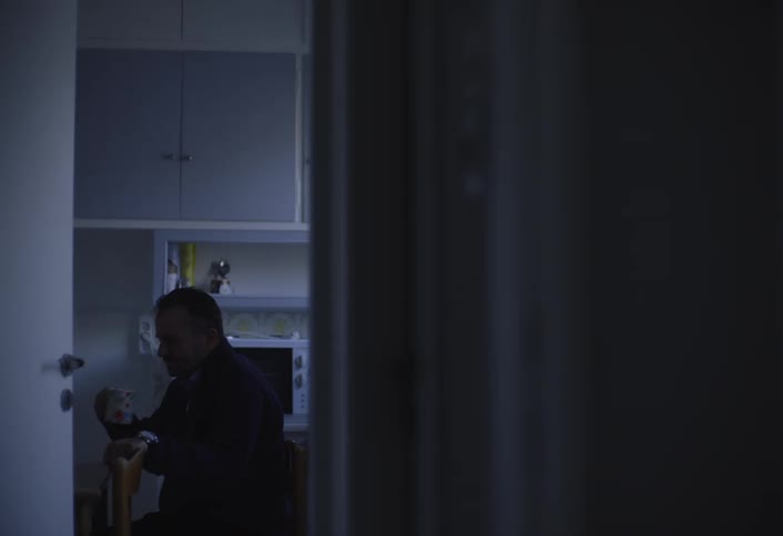 Man sits alone and drinks coffee in dimly lit kitchen