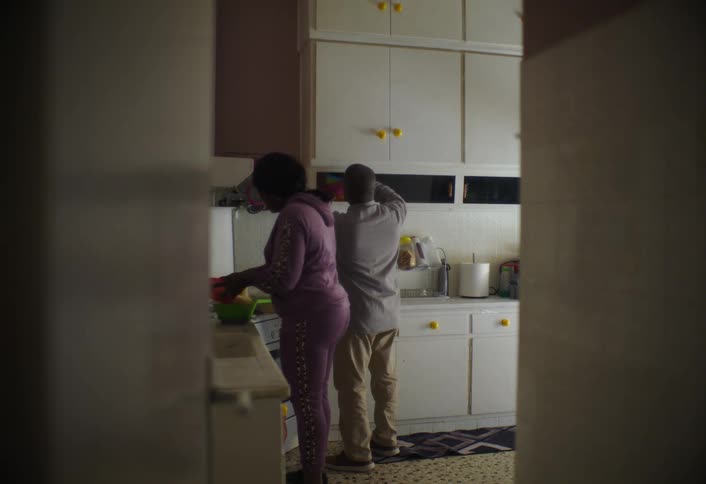 The video shows a man and a woman in a kitchen with the woman on the left wearing pink pajamas and the man on the right wearing a yellow shirt and khaki pants they are both facing away from the camera seemingly engaged in cooking or kitchen activities