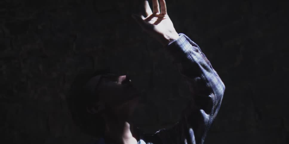 A man reaches upward into a shaft of light shining through a dark stony space