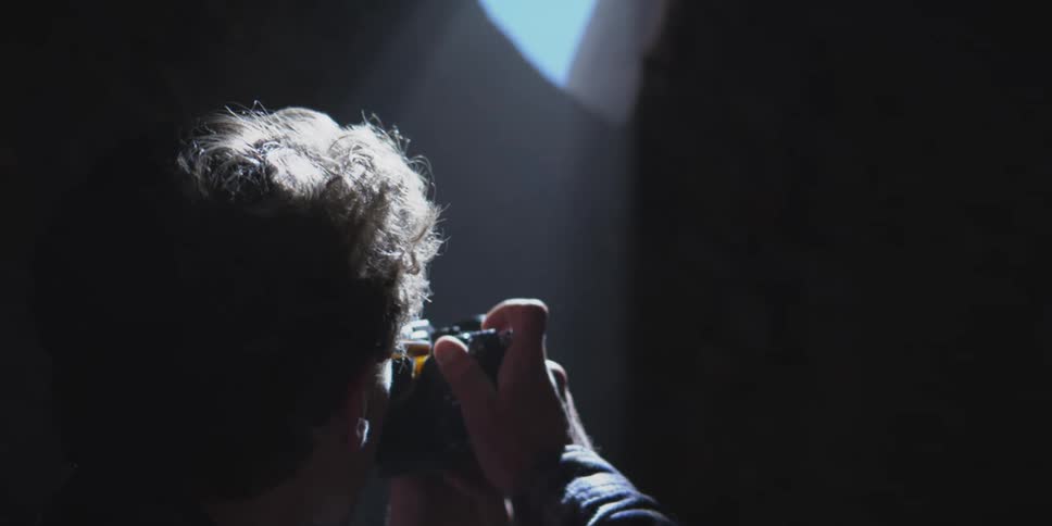 A person photographs upward through a narrow gap in dramatic light