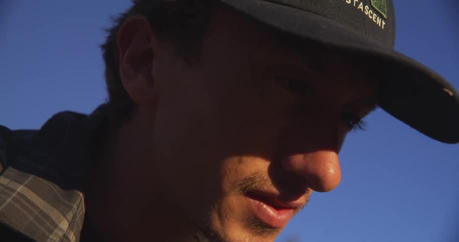 A person in a plaid shirt and cap stands outdoors under a clear blue sky