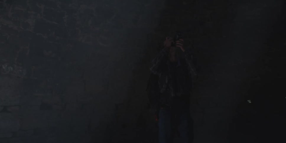 A person holds a camera up toward a light source in a dark stonewalled room