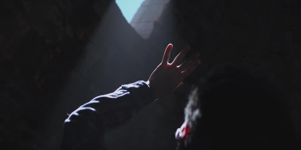 Silhouette of a person looks up toward a sliver of daylight filtering through a narrow rock opening