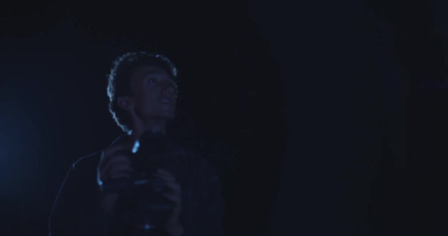 A young man is out in the woods at night taking pictures with his camera for a moment then begins to stare at the sky