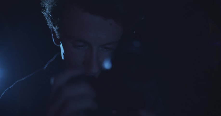 A man looks down at a camera screen in low blue lighting