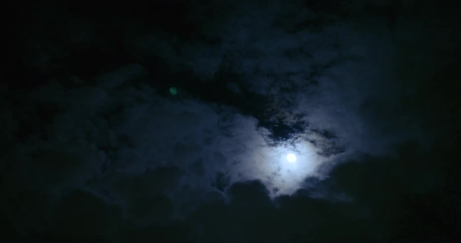 The moon moving above dark clouds in the night sky