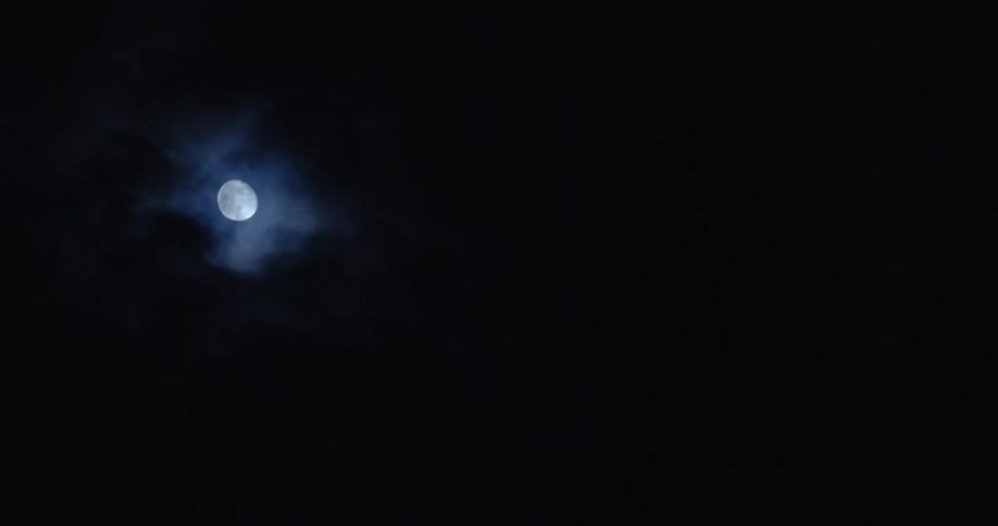 A bright moon in the dark sky with clouds passing in front