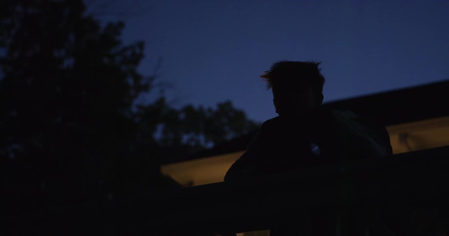 A person stands outdoors at night holding a flashlight a house in the background