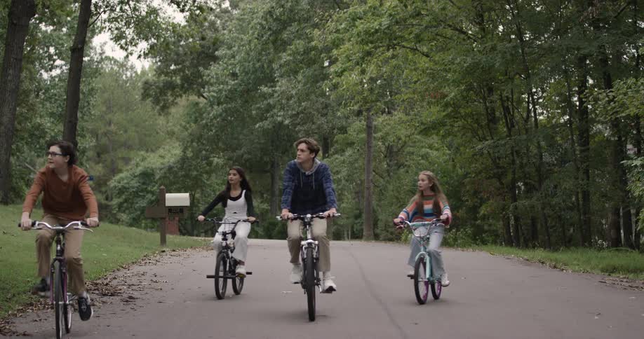 Teenagers and children riding bikes through a wooded park