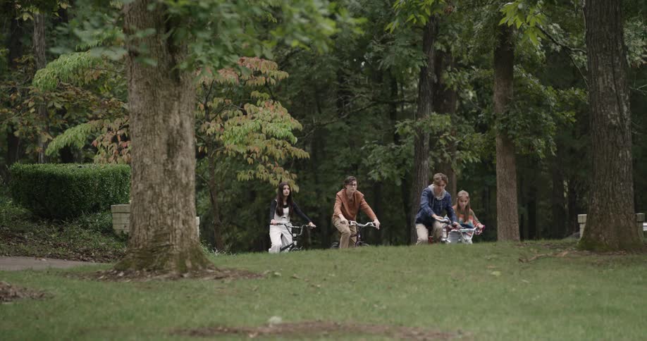 Four teenagers are cycling in the park at midday