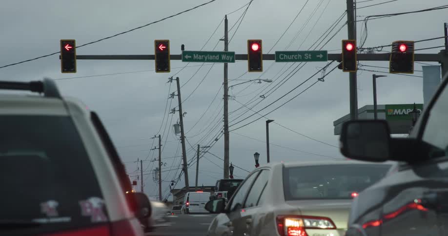 Cars wait at a red light at a city intersection under an overcast sky