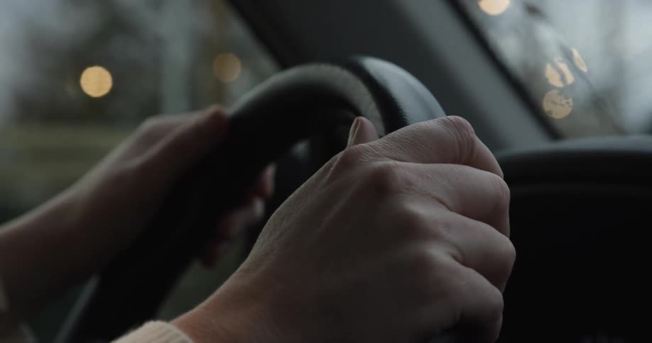 A persons arm is holding the steering wheel while driving through the city at midday