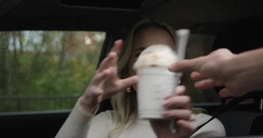 A person in a car receives a drink from a drivethru employee through a service window