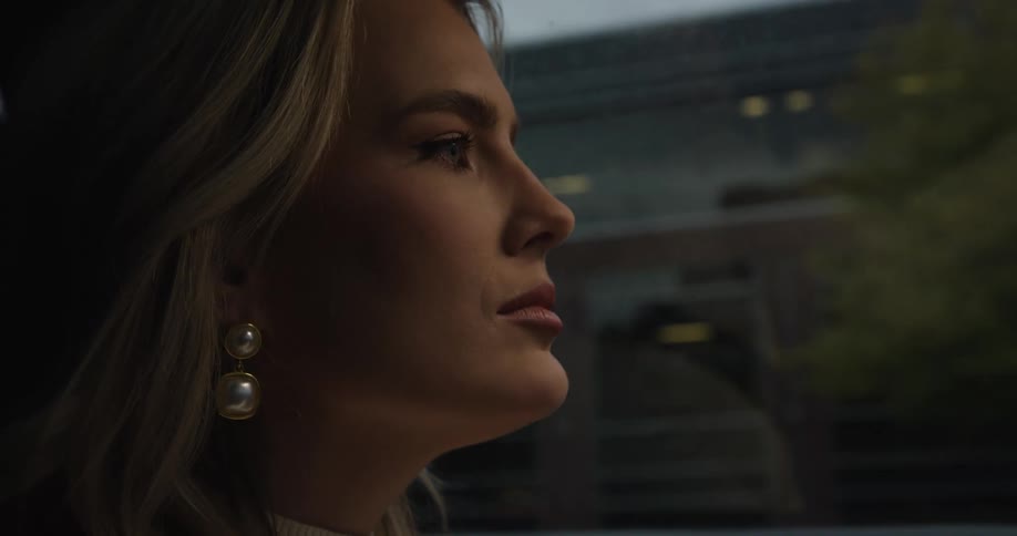 A woman with pearl earrings gazes pensively out of a window as soft light falls on her face