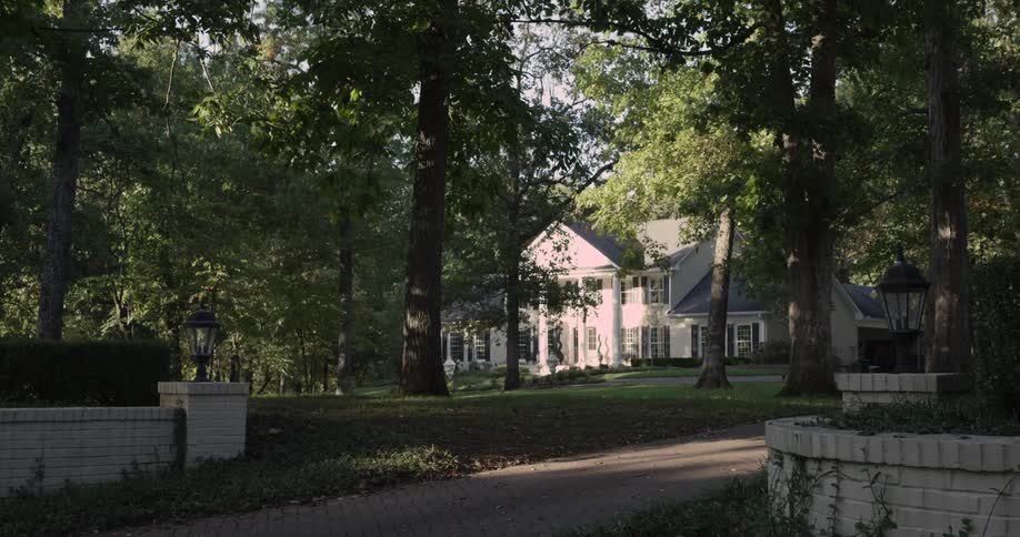 A peaceful suburban home painted light pink is nestled among tall green trees in a wooded neighborhood
