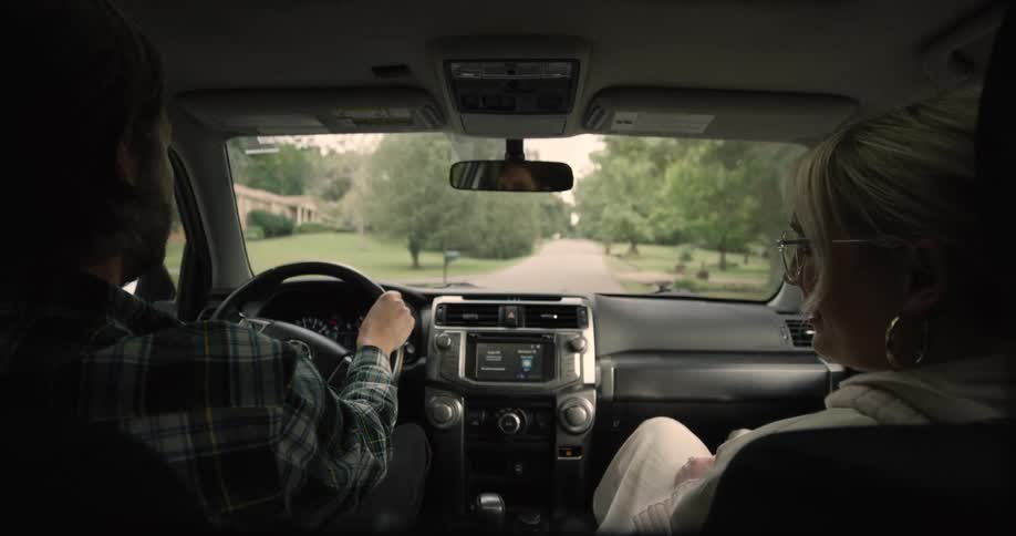 A man is driving a car with a woman beside him and they are engaged in a conversation as they drive at midday