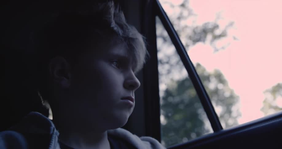 A teenage boy sitting in the back of a car opens the door and steps out after the car comes to a stop