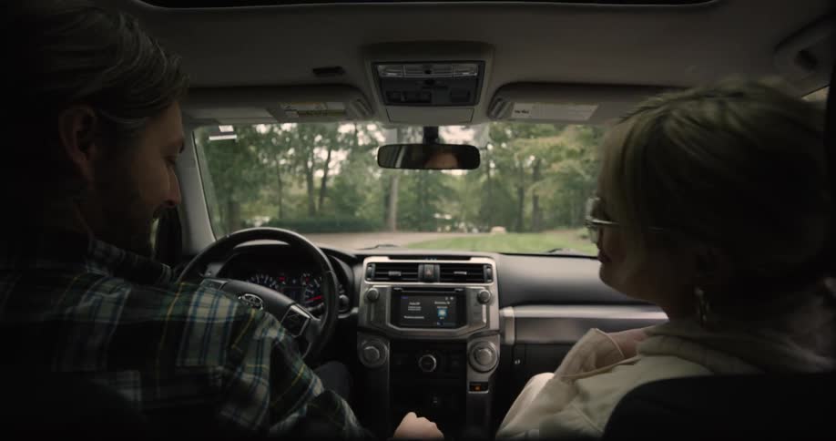 A couple drives into their driveway engaged in conversation and both exit the car at the same time walking toward their house at midday
