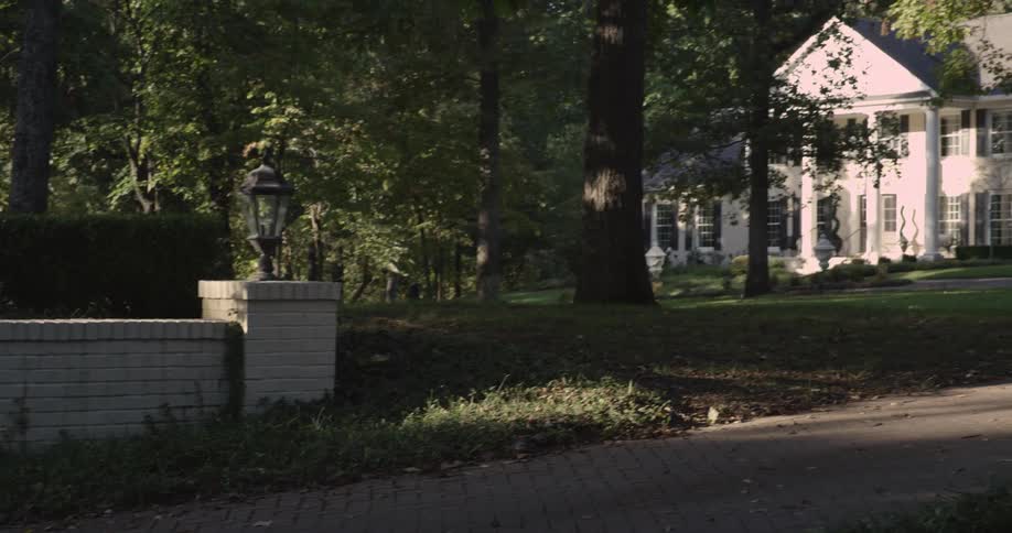 A colonial style house sits quietly among tall trees in suburbia