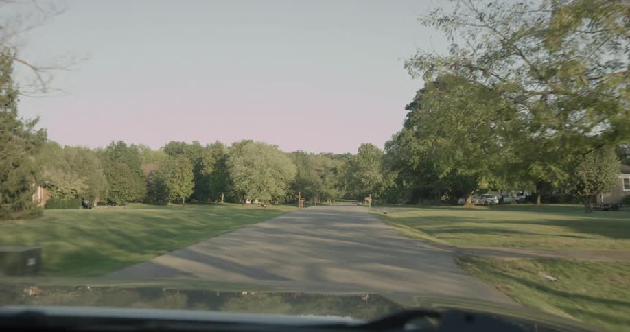 Point of view of a car moving along a road in a residential neighborhood surrounded by trees