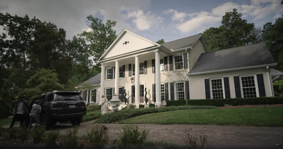 A family exits a black suv and walks toward a large white suburban house